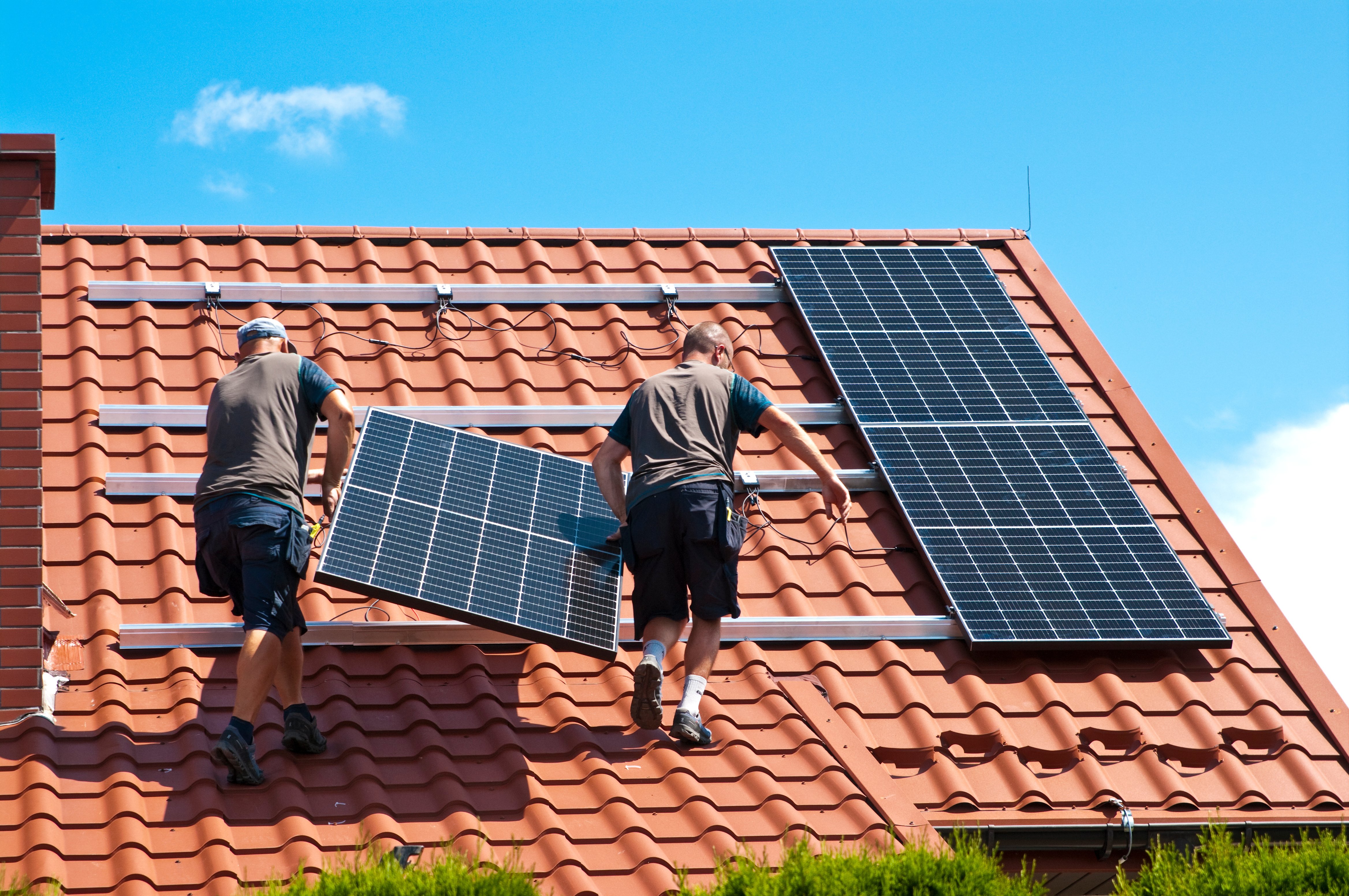 Two installers mounting solar panels on a red tile roof in New Zealand – World Solar installation